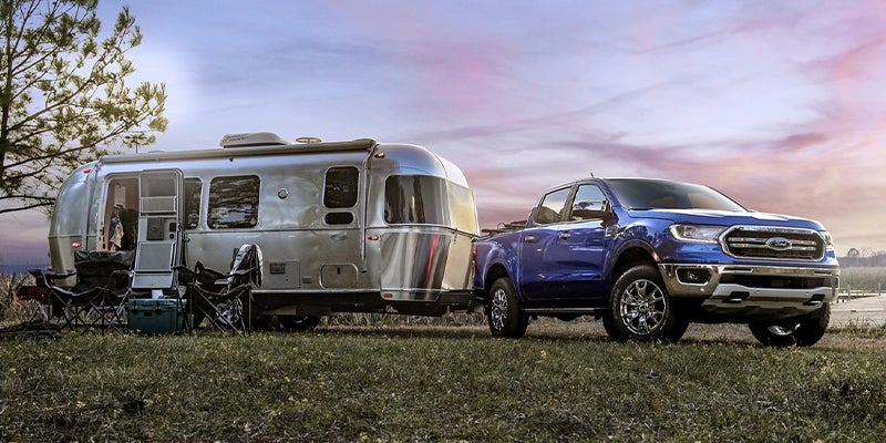 Blue 2023 Ford Ranger parked with a camper hitched and beautiful skies behind