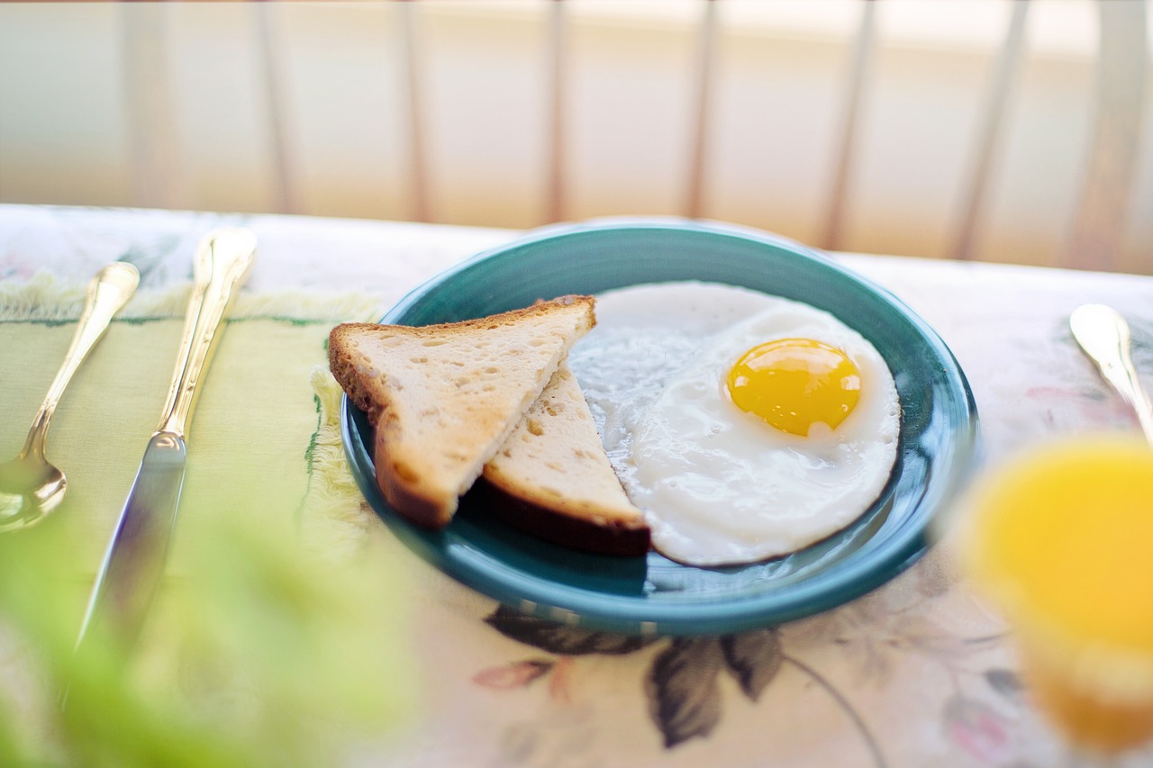 sunny side up egg and toast on a blue plate with silverware to the left and a glass of orange juice to the right