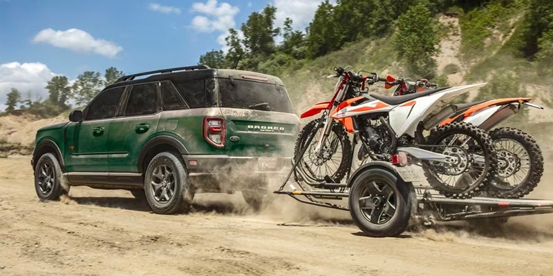 A green 2024 Ford Bronco Sport hauling a trailer with 2 dirt bikes secured