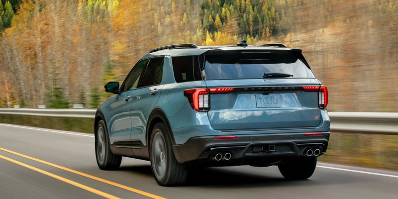 Blue Ford Explorer SUV driving on a road with a scenic autumn background.