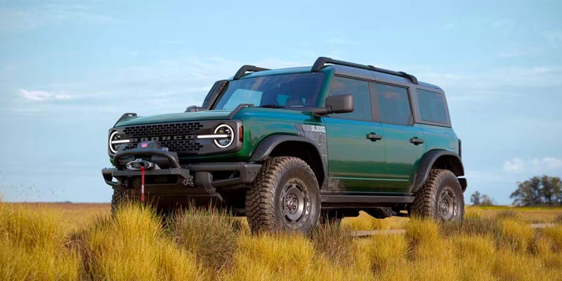 Green 2024 Ford Bronco parked on grassy terrain with a clear blue sky in the background