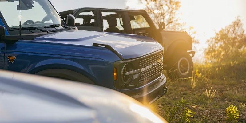 View of the hoods of 3 2024 Ford Broncos parked next to one another with the sun setting in the background