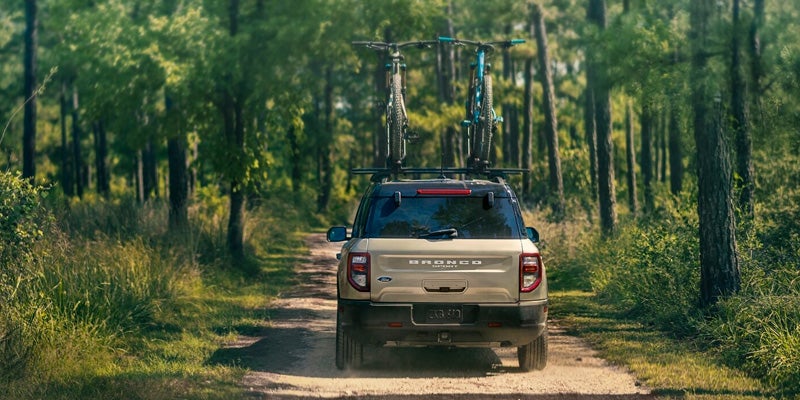 Rear view of a tan 2024 Ford Bronco Sport driving down a dirt road on a sunny day